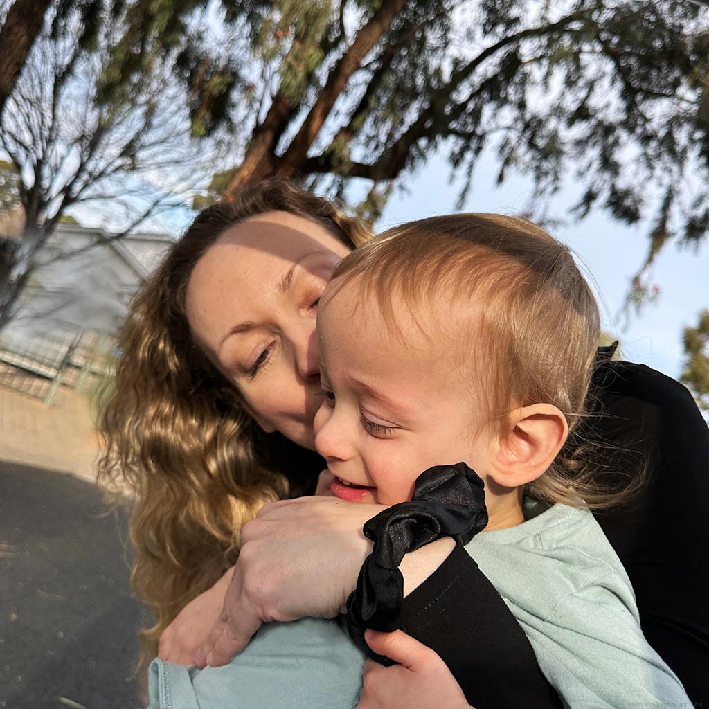 Woman holding a child outdoors with trees in the background